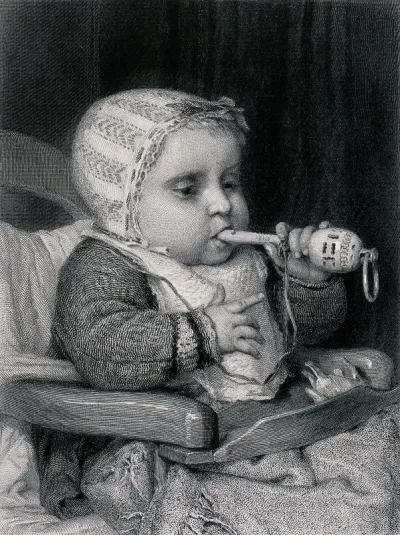 A baby sits in a chair chewing a rattle