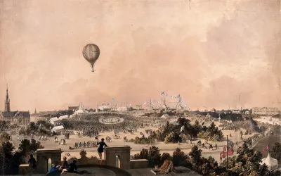 A balloon flies over a park with marquees and bunting where crowds of people are gathered