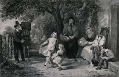 A boy grinds a barrel organ as two small girls dance to amuse another child who is leaning against pillows in a chair