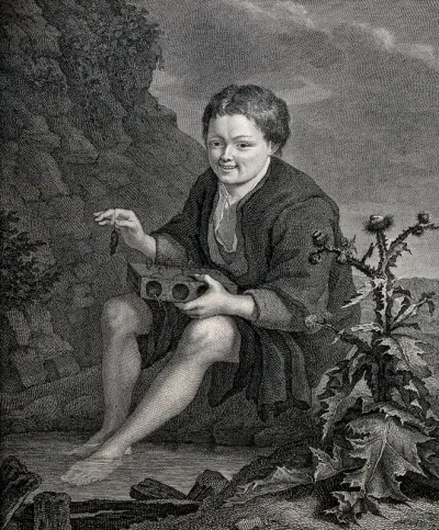 A boy holding a mouse trap on his knees and a dead mouse in his right hand sits with his feet immersed in a pool