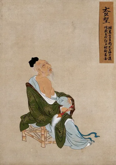 A Chinese figure, seated on a bamboo chair, wearing green coloured silk robes with a brown border; pictured with a flywhisk