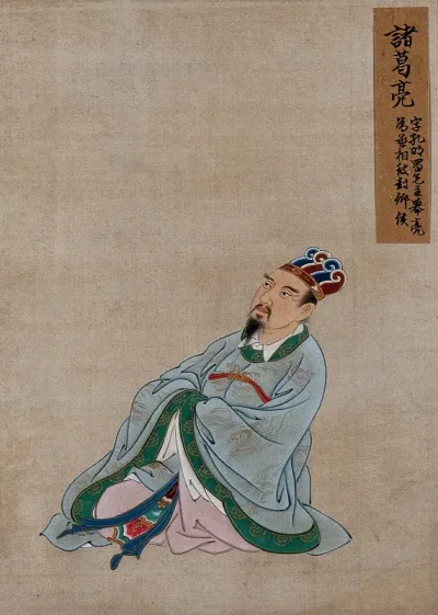 A Chinese figure wearing pale blue silk robes with a emerald green border and elaborate head-dress