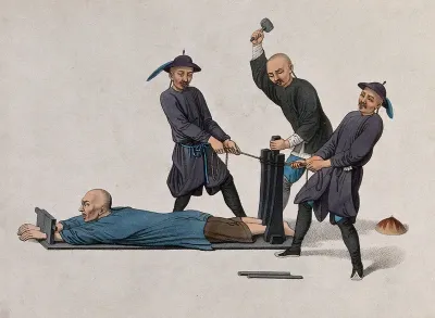 A Chinese man is lying on an horizontal pillory while two Chinese men are tying a rope around the wooden structure at its base and a third man is hammering on a pole in order to crush the victim's ankles