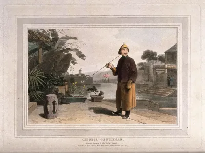 A Chinese man stands in his garden smoking a long-stemmed pipe