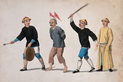 A Chinese man with his hands bound behind his back and two red flags on his head is being whipped with wooden sticks, as he is led to trial by a man beating a gong