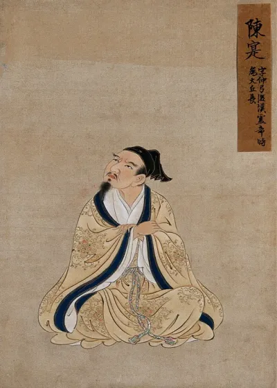 A Chinese seated figure, full frontal, with grey beard, buff coloured robes with a blue border and wearing a black cap