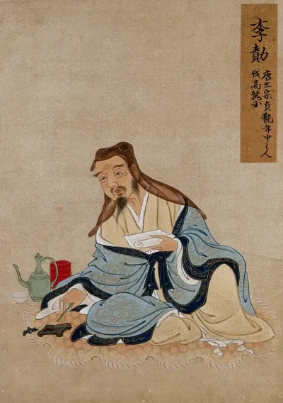 A Chinese seated figure with grey beard and black hat, with pen and paper