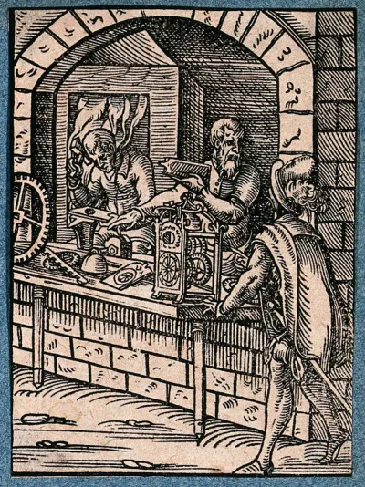 A clock-maker is talking to a man outside his shop as he assembles a clock and an assistant works beyond