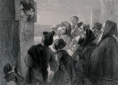 A crowd of people have gathered around a stand in the street to watch a Punch and Judy show