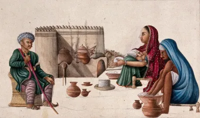 A high ranking man sitting in front of a couple preparing chappatis (bread) and the woman nursing her baby