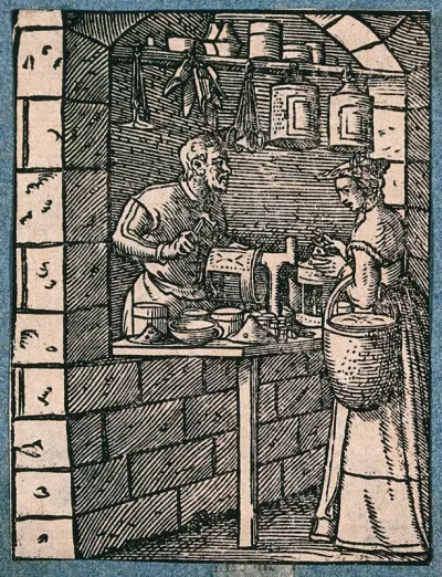 A lantern maker working at his bench, talking to a woman customer who inspects a finished lantern