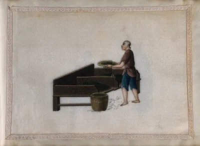 A man grading (?) tea leaves by sieving them into one of two compartments in a special work table
