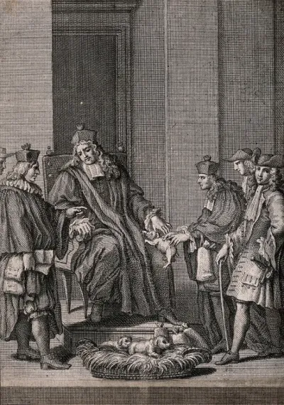 A man in a clerical cloak and hat is sitting on a chair as a puppy is handed to him from a basket on the floor at his feet