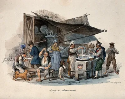 A man is cooking macaroni under a large awning in the street, his customers are sitting on benches enjoying their food