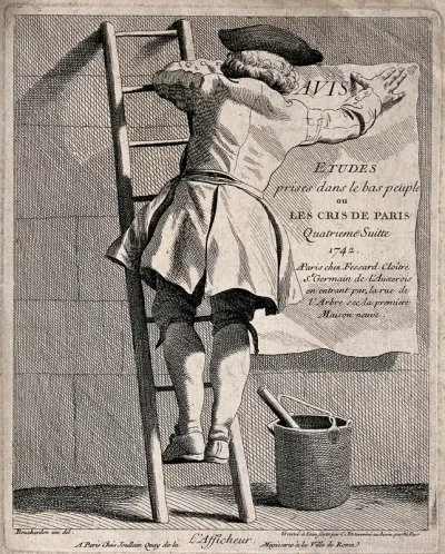 A man is standing on a ladder, with a pot of paste on the ground as he sticks a poster to the wall