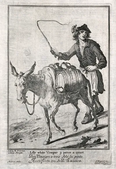 A man is whipping a donkey on as it carries the panniers which hold the vinegar that he will sell