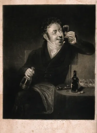 A man sits by a table and examines a full glass of wine that he holds to the light