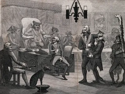 A man sits on a high chair in front of a table surrounded by others: they watch two men in the middle of the floor perform a ritual