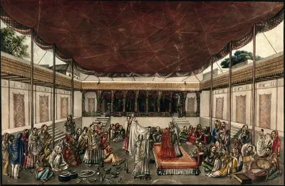 A marriage ceremony: the bride, in red, stands on a raised platform and is hiding from the groom behind a white sheet