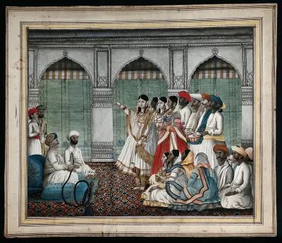 A Nawab (?) holding a hookah pipe, as a woman dances in front of him, watched by some musicians and a group of people