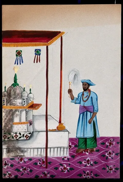 A small mosque under a canopy being attended to by a man holding a fly whisk