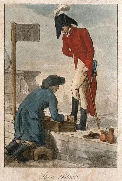 A soldier in uniform is having his boots cleaned in the street by a man kneeling in a box