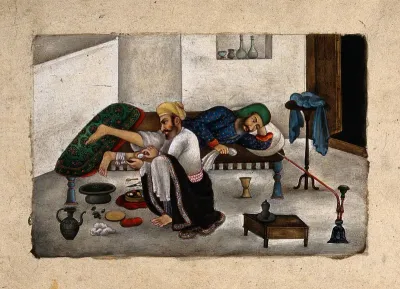 A surgeon, sitting on the floor, attends to a patient's leg, as he lies on a bed