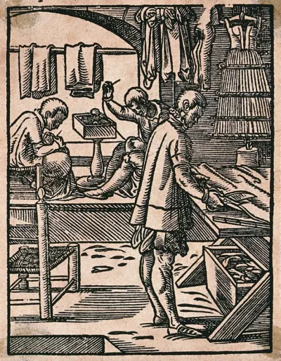 A tailor cutting cloth with scissors while his colleagues sew at a bench