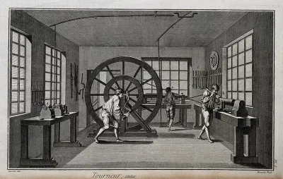 A turner's workshop, a man working the crank of a large lathe, tools ranged around the walls