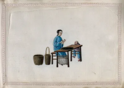 A woman examining a shallow basket of tea leaves laid on a table, watched by a small boy