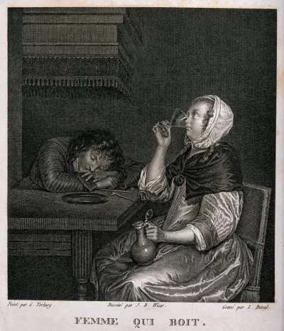 A woman sits drinking as a man sleeps with his head on the table beside her
