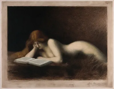 A woman with long red hair is lying down reading a book