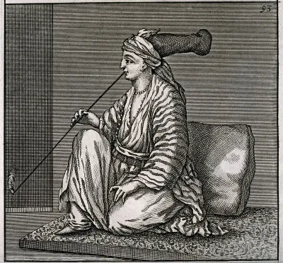 A young Jewish woman with long-crowned turban kneels on a mat smoking opium
