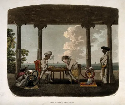 An Englishman and Asian man seated in a pavilion playing chess and both smoking the hooka