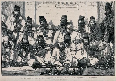 Fourteen male prisoners in Persia sitting on the ground in a group bound together at the neck by chains, with an armed guard