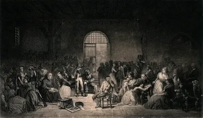 French Revolution: a prisoner sits in the middle of a crowded prison room as a woman nearby pleads with an official