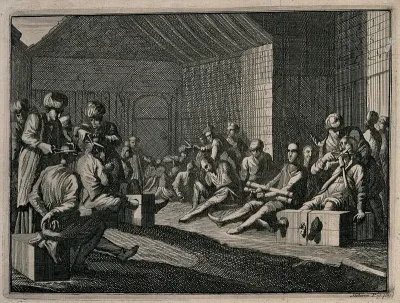 Male prisoners are sitting with their legs in stocks and their hands tied as men in turbans cut off their hair and moustaches