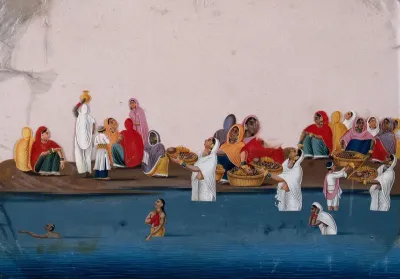 People bathing and praying in the Ganges, while a group of women sit on the shore selling religious items