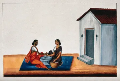 Two Indian women working on the quern to grind the grain into flour
