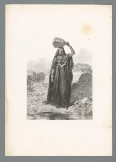 Vrouw met opvallende sieraden en hoofddoek aan de waterkant met waterkruik op haar hoofd